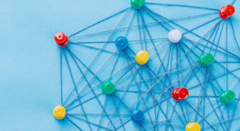 Small network of pins (Thumbtack)and string, An arrangement of colorful pins linked together with string on a pale blue background suggesting a network of connections.