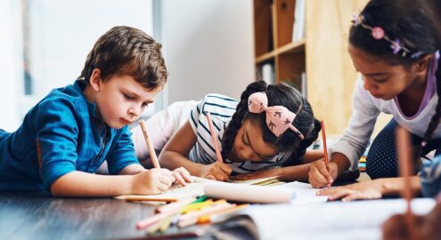 Three children coloring while lying on the floor